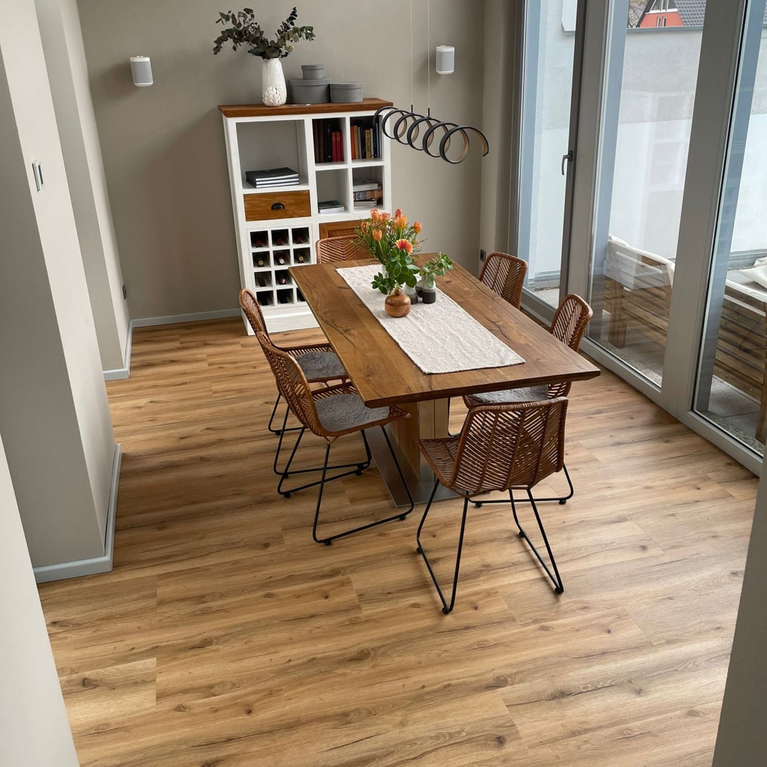 Klick-Vinylboden in Braun in Esszimmer mit Esstisch und braunen Stühlen, Tischdecke, Schrank mit Bucüchern und Pflanzen