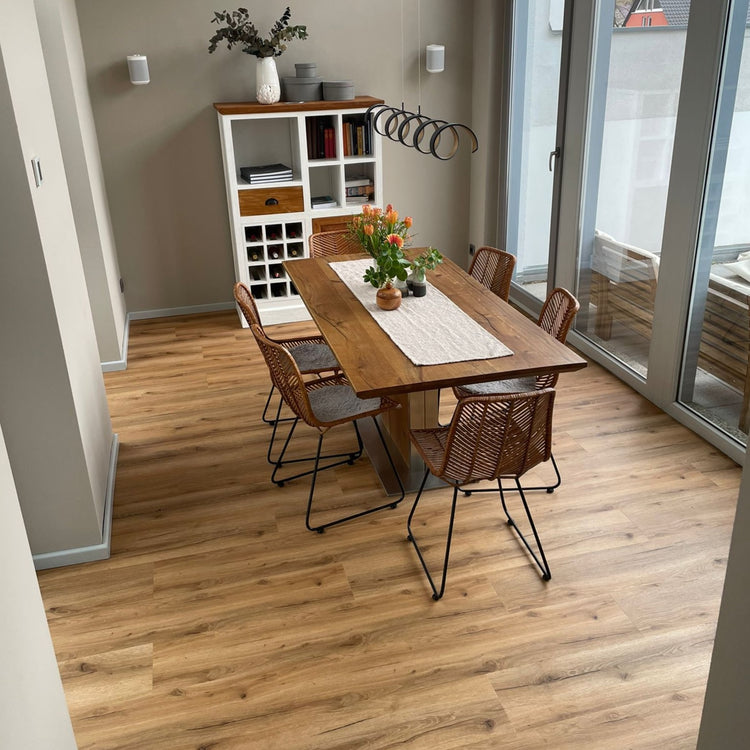 Klick-Vinylboden in Braun in Esszimmer mit Esstisch und braunen Stühlen, Tischdecke, Schrank mit Bucüchern und Pflanzen