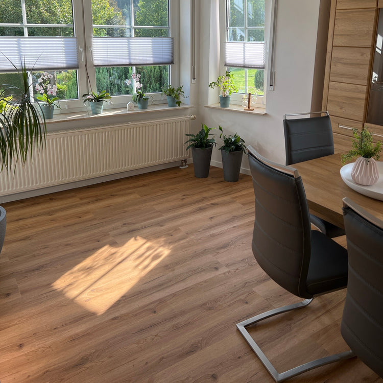 Klick-Vinylboden in Braun in modernem Wohnzimmer mit Tischausschnitt, Stühlen, Pflanzen auf Fensterbrett